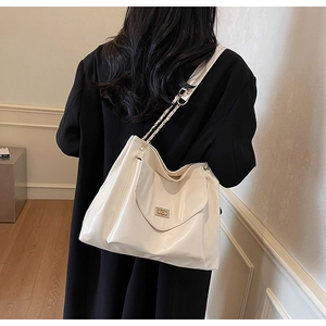 Détail du sac cabas blanc crème avec chaîne en métal et fermoir rotatif sur manteau noir