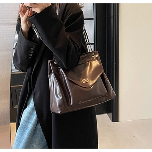 Detail of deep brown leather tote with golden rectangular lock and metal chain strap