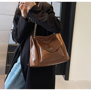 Macro view of dark brown tote bag featuring glossy texture, metal chain and flip buckle