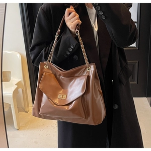 Detail of caramel leather tote bag with gold chain straps and a metal twist-lock buckle
