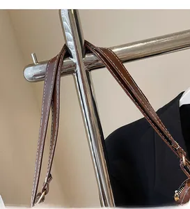 Détail d'une bandoulière en cuir marron foncé avec surpiqûres blanches et boucle dorée
