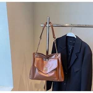 Detail of vintage brown tote bag featuring golden chain strap and metallic twist lock