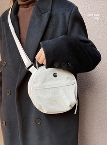 Close-up of white nylon round bag with metal M logo on a black cashmere coat