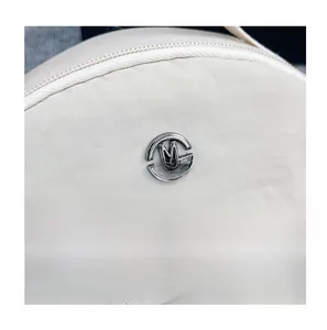 Detail of cream nylon fabric with silver round M FASHION metal logo and neat stitching