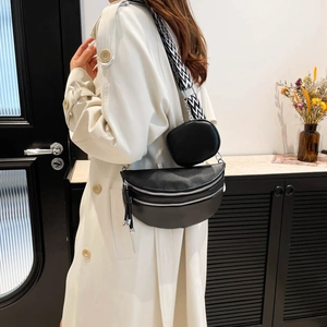Borsa a mezzaluna in pelle nera con tracolla geometrica indossata su un trench beige