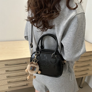 Minimalistische schwarze Umhängetasche aus Glanzleder mit Teddybär-Anhänger und Logo