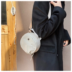 Detail of minimalist cream nylon round crossbody bag worn with a black wool coat
