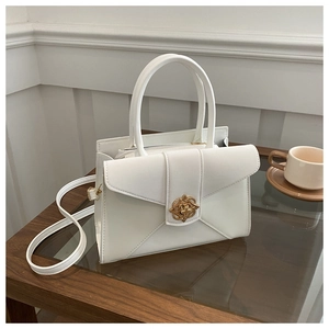 Detail of a creamy white tote bag featuring a golden vintage floral embossed lock closure