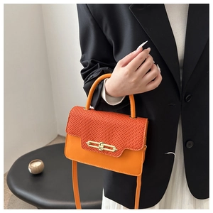 Detail of vibrant orange woven crossbody bag with gold buckle on a minimalist backdrop