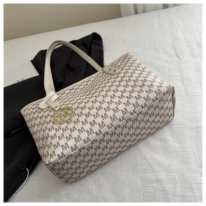 Détail du sac cabas beige avec motif M et breloque en métal doré sur un fond textile doux