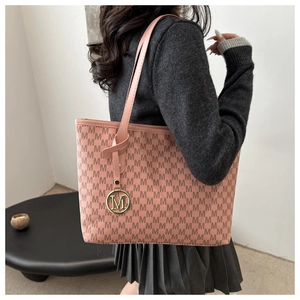 Pink tote bag with letter M monogram pattern and golden metal charm shown on model