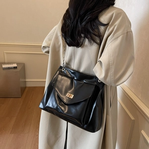 Classic black leather chain tote bag with gold metal lock worn by a model in beige coat