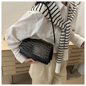 Detail shot of a black shoulder bag showing croc-effect texture and smooth leather finish