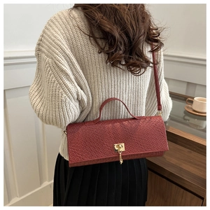 Detail of brick red bag with crocodile pattern and golden rotating square metal clasp