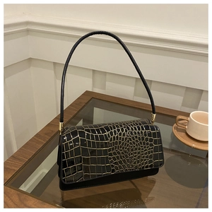 Detail of black faux leather bag with gold crocodile texture flap on glass table