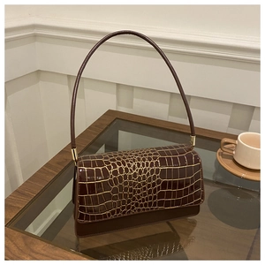 Detail of dark brown faux crocodile leather shoulder bag on a glass table with gold metal hardware