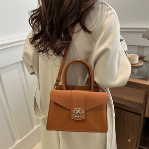 Elegant caramel leather tote bag with floral metal clasp shown in a minimalist home setting