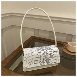 Detail of white crocodile pattern shoulder bag on a cafe table with gold hardware
