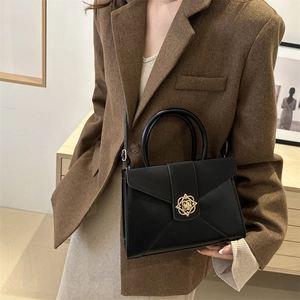 Minimalist black matte leather tote bag with gold geometric flower clasp on brown blazer