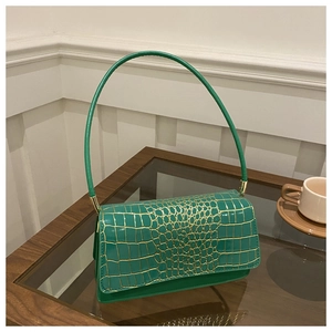 Detail of dark green crocodile pattern handbag with golden metal hardware and flap closure