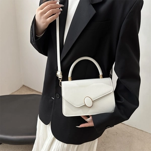 Piccola borsa quadrata in pelle bianca con chiusura dorata su un blazer nero