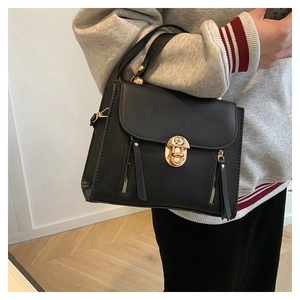 Détail du sac à main noir avec fermoir doré porté par un mannequin en sweat-shirt gris