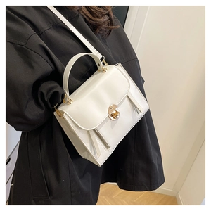 Détails d'un sac à main blanc structuré avec ferrures dorées sur un manteau noir