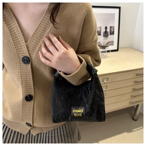 Detail of black pleated fabric handbag featuring yellow mIAO SHE logo patch and leather handle