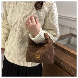 Close-up of brown pleated mini tote with knotted handle and brand logo patch