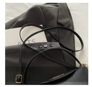 Close-up of black litchi grain leather shoulder bag with adjustable gold buckle strap