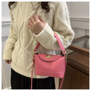 Close-up of pink crossbody bag with lychee texture and gold twist lock on knit sweater