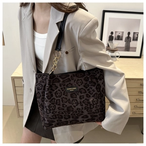 Detail of leopard print tote bag featuring a black logo plate and gold chain strap accents
