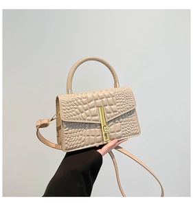 Close-up of beige crocodile pattern handbag with gold metal clasp and top handle detail