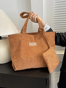 Brown corduroy tote bag with fashion label and small zipper pouch in warm indoor light
