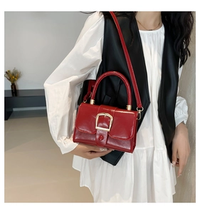 Detail of red patent leather mini bag with gold buckle and crossbody strap shown on model