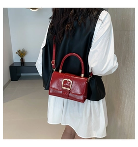 Detail of red patent leather square handbag with gold buckle and adjustable strap