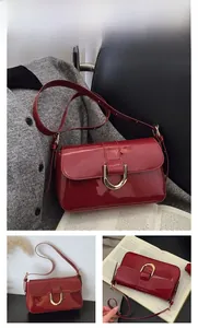Detail of wine red patent leather shoulder bag with gold metal buckle and glossy finish