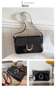 Detail of black patent leather shoulder bag with gold horseshoe buckle and strap