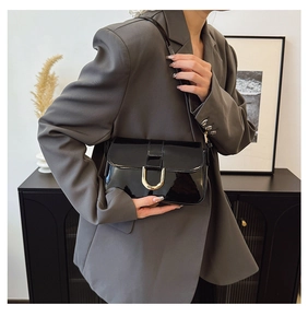 Detail of glossy black patent leather underarm bag with gold D-ring buckle and flap