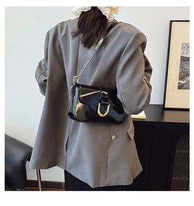 Detail of black glossy shoulder bag featuring iconic gold horseshoe buckle on sleek flap