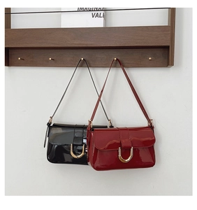 Detail of glossy patent leather shoulder bags in black and burgundy with gold buckles