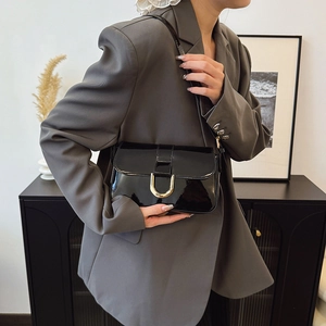 Elegant black patent leather shoulder bag with gold horseshoe buckle on casual blazer