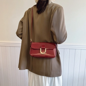 Red patent leather crossbody bag with golden U-shaped buckle shown on a model