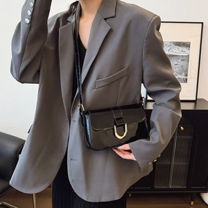 Glossy black patent leather shoulder bag with gold buckle worn with a grey blazer
