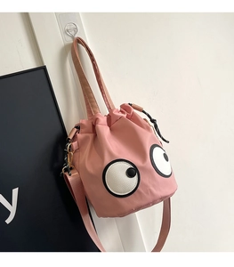 Detail of pink nylon bucket bag with large cartoon eyes and drawstring closure