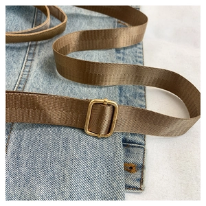 Detail of adjustable brown nylon shoulder strap with gold metal buckle on denim fabric