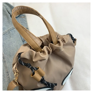 Close-up of khaki nylon tote bag with cartoon eye appliqué and plaid drawstring detail