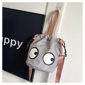 Detail of grey nylon bucket bag featuring large cartoon eyes and pink shoulder straps
