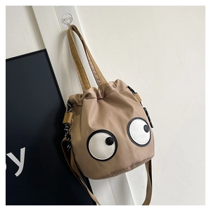 Detail of a beige nylon bucket bag with large cartoon eyes hanging on a white door