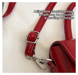 Détail du sac en cuir rouge montrant la bandoulière réglable et la boucle en métal argenté